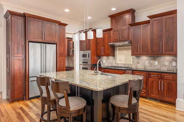 kitchen featuring a center island with sink, appliances with stainless steel finishes, light stone counters, decorative backsplash, and sink