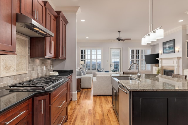 kitchen with ceiling fan, stainless steel appliances, an island with sink, and ornamental molding