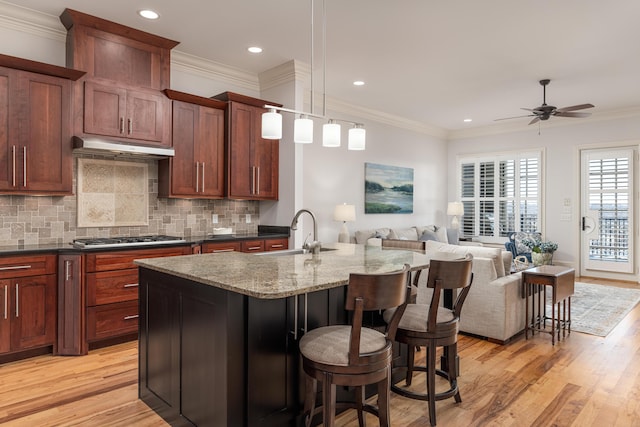 kitchen featuring a center island with sink, stainless steel gas cooktop, a breakfast bar, light stone counters, and sink