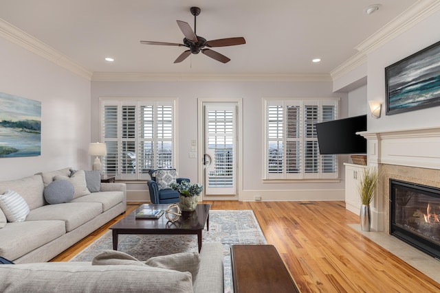 living room with a fireplace, ceiling fan, light hardwood / wood-style flooring, and ornamental molding