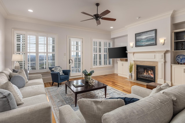 living room with ceiling fan, light wood-type flooring, crown molding, and a fireplace