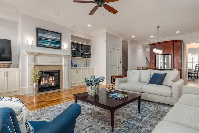 living room featuring built in shelves, ceiling fan, light hardwood / wood-style floors, and ornamental molding