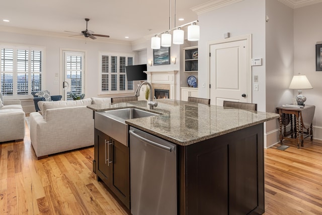 kitchen featuring light stone counters, dishwasher, an island with sink, ceiling fan, and sink