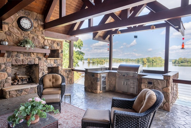 view of patio featuring a grill, an outdoor stone fireplace, exterior kitchen, a gazebo, and a water view