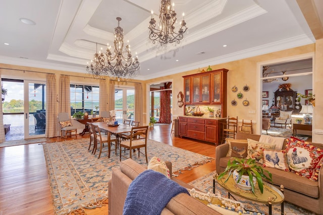 dining area with ornamental molding, a notable chandelier, light hardwood / wood-style floors, a raised ceiling, and french doors