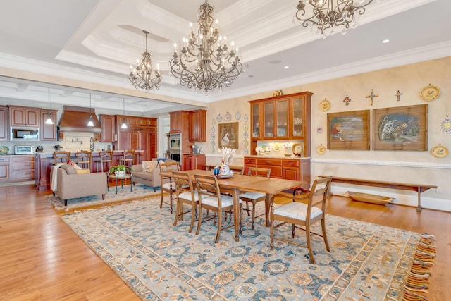 dining room with a raised ceiling, crown molding, light wood-type flooring, and an inviting chandelier