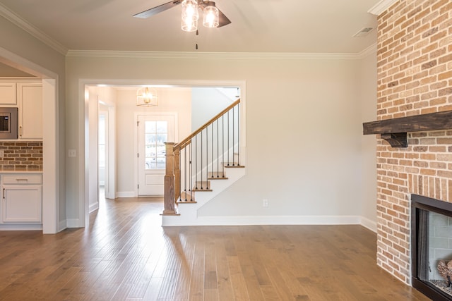 unfurnished living room featuring ornamental molding, a brick fireplace, wood-type flooring, and ceiling fan