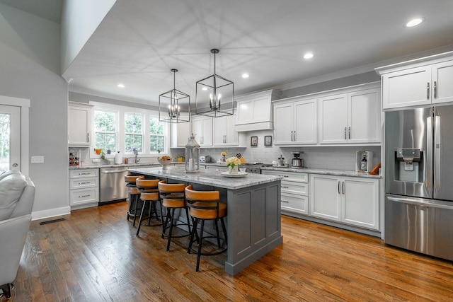 kitchen featuring appliances with stainless steel finishes, white cabinetry, light stone counters, a center island, and decorative light fixtures