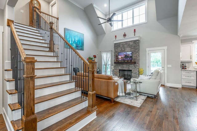 living room featuring ceiling fan, a stone fireplace, a towering ceiling, and dark wood-type flooring