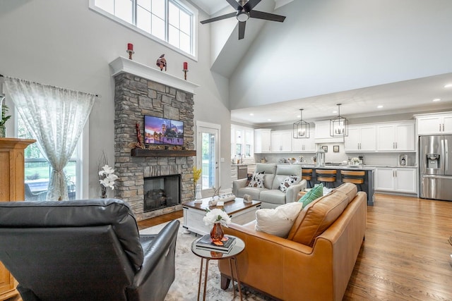 living room with ceiling fan with notable chandelier, a high ceiling, a fireplace, and light hardwood / wood-style flooring