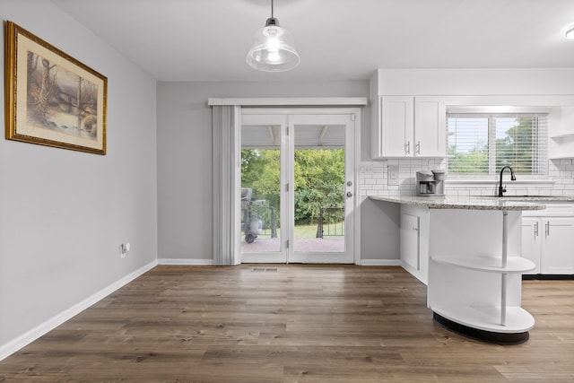 kitchen with decorative light fixtures, white cabinetry, light stone countertops, and a wealth of natural light