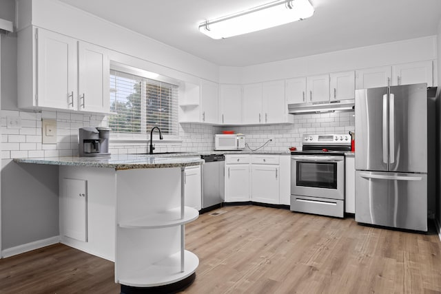 kitchen featuring appliances with stainless steel finishes, tasteful backsplash, white cabinets, light stone countertops, and light hardwood / wood-style flooring