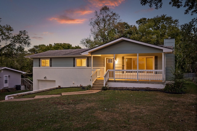 view of front of home with a yard, covered porch, central air condition unit, and a garage