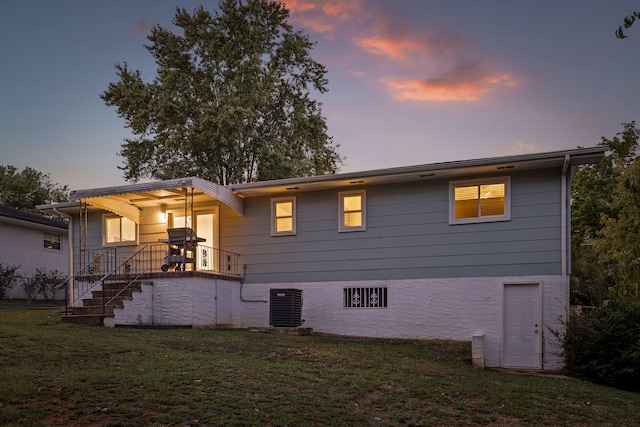 back house at dusk featuring a lawn and cooling unit