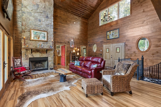 living room featuring a notable chandelier, high vaulted ceiling, hardwood / wood-style flooring, and a stone fireplace