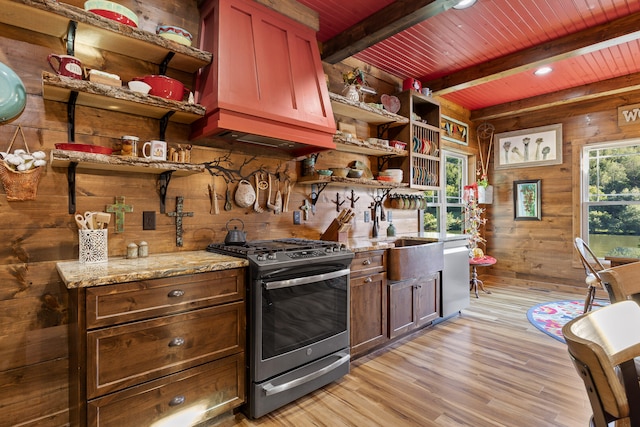 kitchen with wood walls, beamed ceiling, light wood-type flooring, light stone counters, and appliances with stainless steel finishes