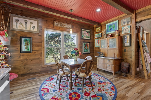 dining area featuring beamed ceiling, light hardwood / wood-style flooring, and wooden walls