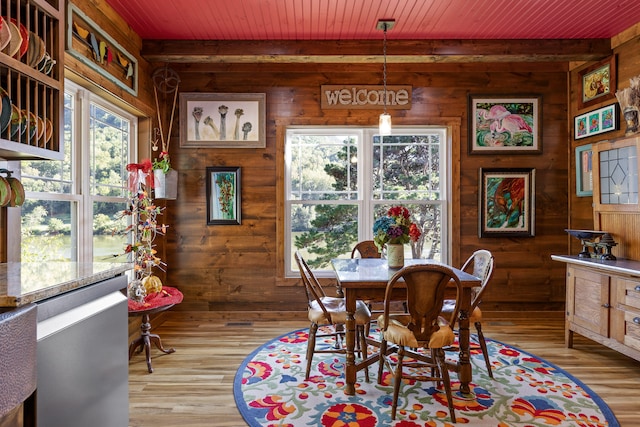 dining area with wood walls, wood ceiling, hardwood / wood-style floors, and beam ceiling