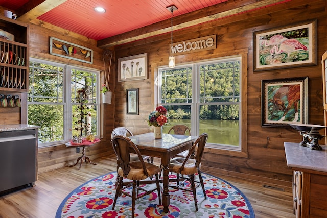 dining area with beamed ceiling, light hardwood / wood-style flooring, wooden walls, and wooden ceiling