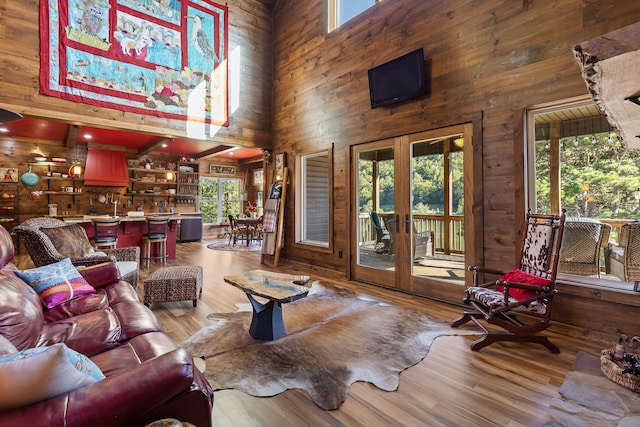 living room featuring french doors, light hardwood / wood-style flooring, wood walls, and a high ceiling