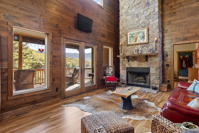 living room with french doors, a stone fireplace, wooden walls, hardwood / wood-style flooring, and a towering ceiling