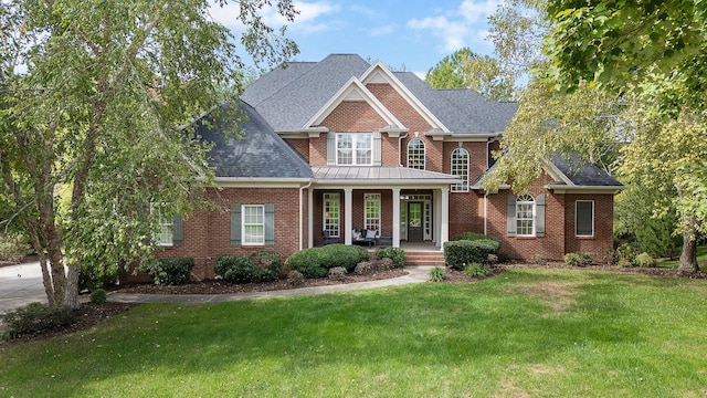 view of front of house with a porch, brick siding, a front yard, and a shingled roof
