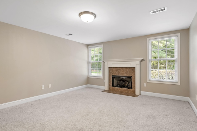 unfurnished living room with light carpet, a tile fireplace, and plenty of natural light