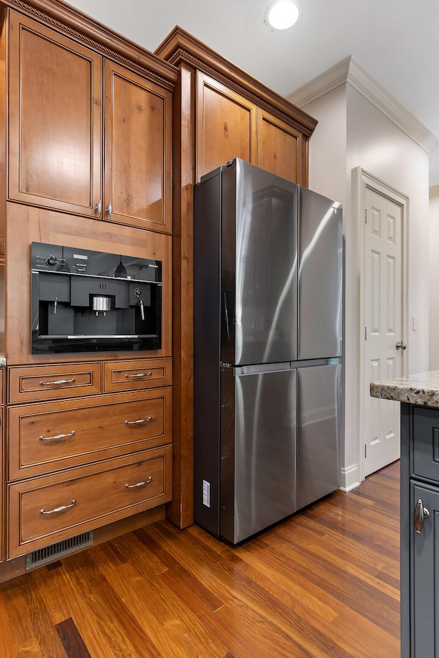 kitchen featuring dark stone counters, crown molding, dark wood-type flooring, and stainless steel refrigerator