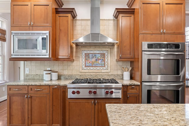 kitchen featuring appliances with stainless steel finishes, decorative backsplash, wall chimney range hood, and light stone counters