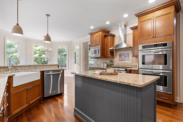 kitchen with appliances with stainless steel finishes, hanging light fixtures, crown molding, hardwood / wood-style flooring, and wall chimney range hood