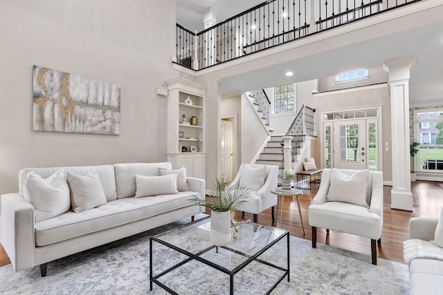 living room featuring a towering ceiling, wood-type flooring, decorative columns, and built in shelves