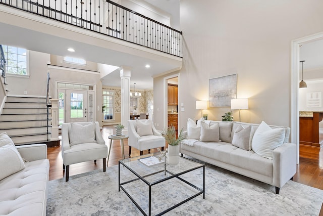 living room with light wood-type flooring, a chandelier, crown molding, a high ceiling, and ornate columns