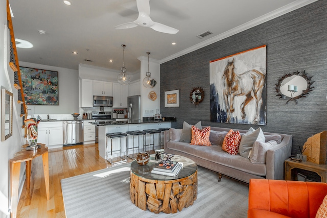 living room with light hardwood / wood-style flooring, ceiling fan, sink, and crown molding