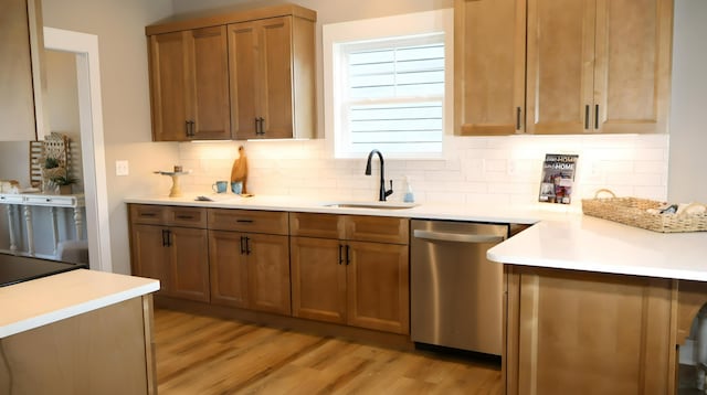 kitchen with tasteful backsplash, stainless steel dishwasher, sink, and light hardwood / wood-style flooring