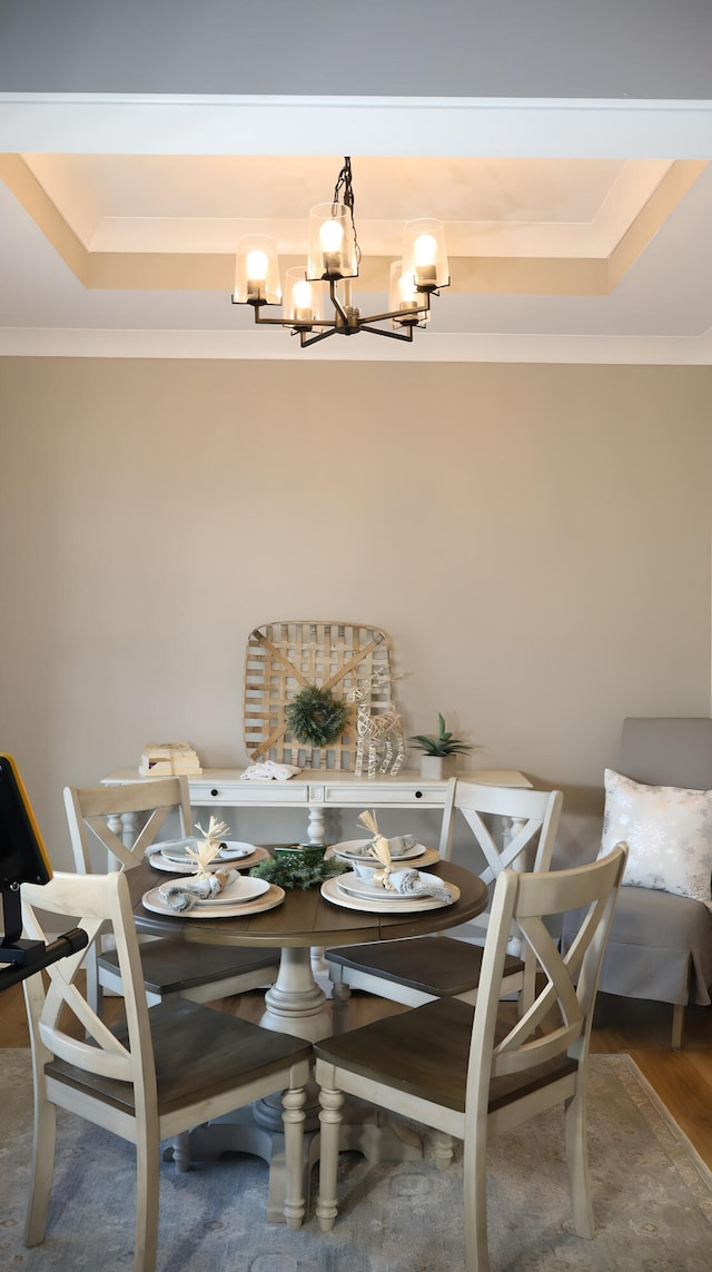 dining area featuring wood-type flooring, an inviting chandelier, crown molding, and a raised ceiling