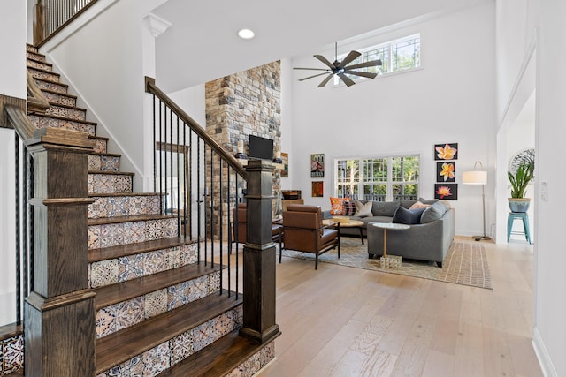 stairs with ceiling fan, a high ceiling, and hardwood / wood-style flooring