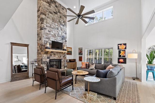 living room with ceiling fan, a stone fireplace, light wood-type flooring, and a towering ceiling