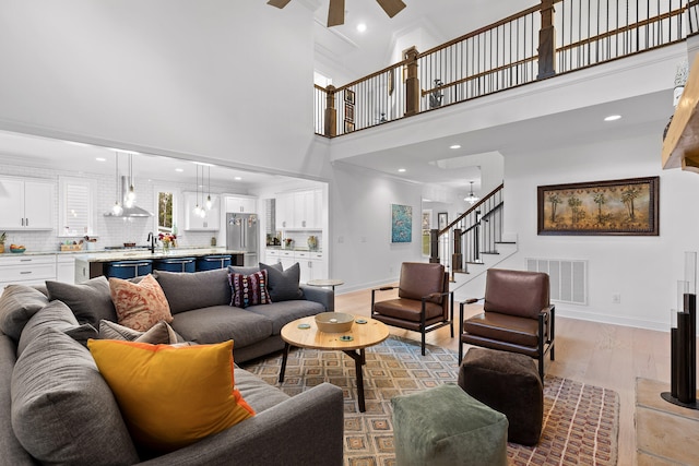 living room featuring ceiling fan, light wood-type flooring, crown molding, and a towering ceiling