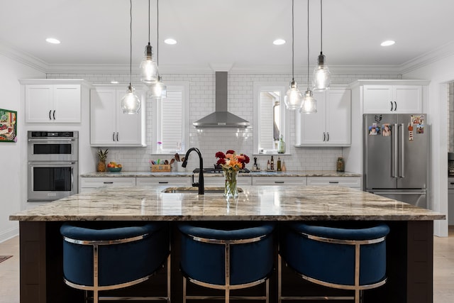 kitchen with a center island with sink, wall chimney exhaust hood, white cabinetry, and appliances with stainless steel finishes