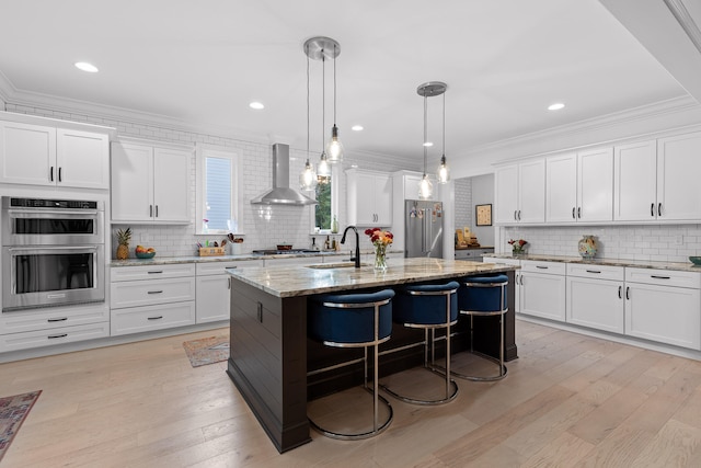 kitchen featuring white cabinetry, a kitchen island with sink, stainless steel appliances, and wall chimney range hood