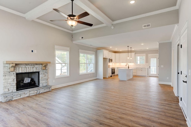 unfurnished living room featuring light wood-type flooring, ceiling fan, sink, beam ceiling, and a fireplace