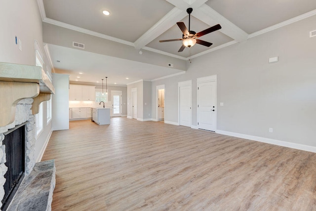 unfurnished living room with light wood-type flooring, ornamental molding, ceiling fan, beam ceiling, and a fireplace