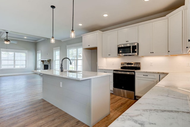 kitchen with white cabinets, appliances with stainless steel finishes, decorative light fixtures, light wood-type flooring, and light stone counters