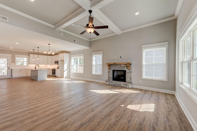 unfurnished living room with beamed ceiling, ceiling fan with notable chandelier, a healthy amount of sunlight, and light hardwood / wood-style flooring