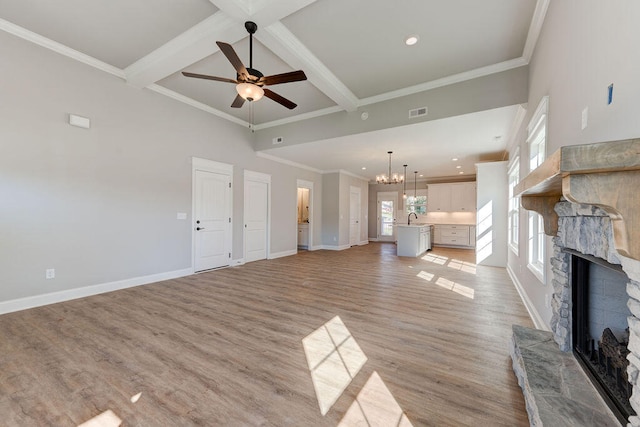 unfurnished living room with sink, beamed ceiling, a fireplace, ceiling fan with notable chandelier, and light wood-type flooring