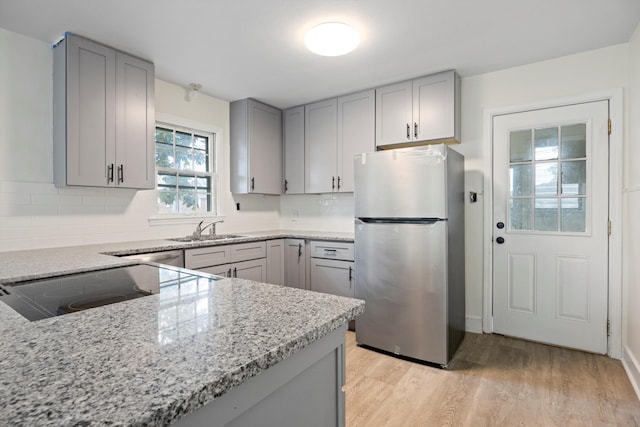 kitchen with light wood-type flooring, light stone countertops, stainless steel fridge, and gray cabinets