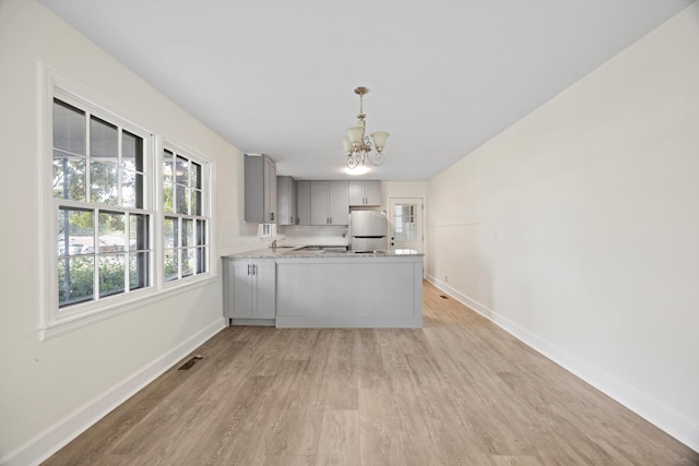 kitchen with light hardwood / wood-style floors, kitchen peninsula, hanging light fixtures, white fridge, and gray cabinetry