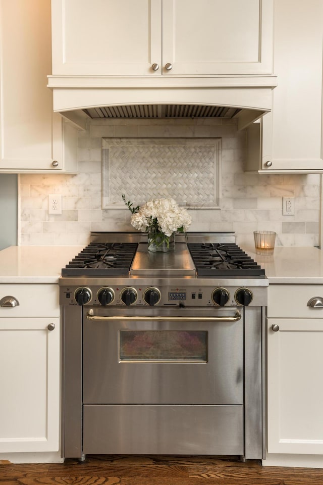 kitchen featuring custom range hood, decorative backsplash, white cabinets, and stainless steel range