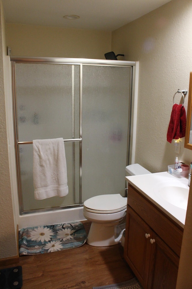 bathroom with wood-type flooring, a shower with door, toilet, and vanity