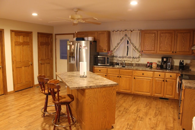 kitchen featuring appliances with stainless steel finishes, light wood-type flooring, a center island, and sink